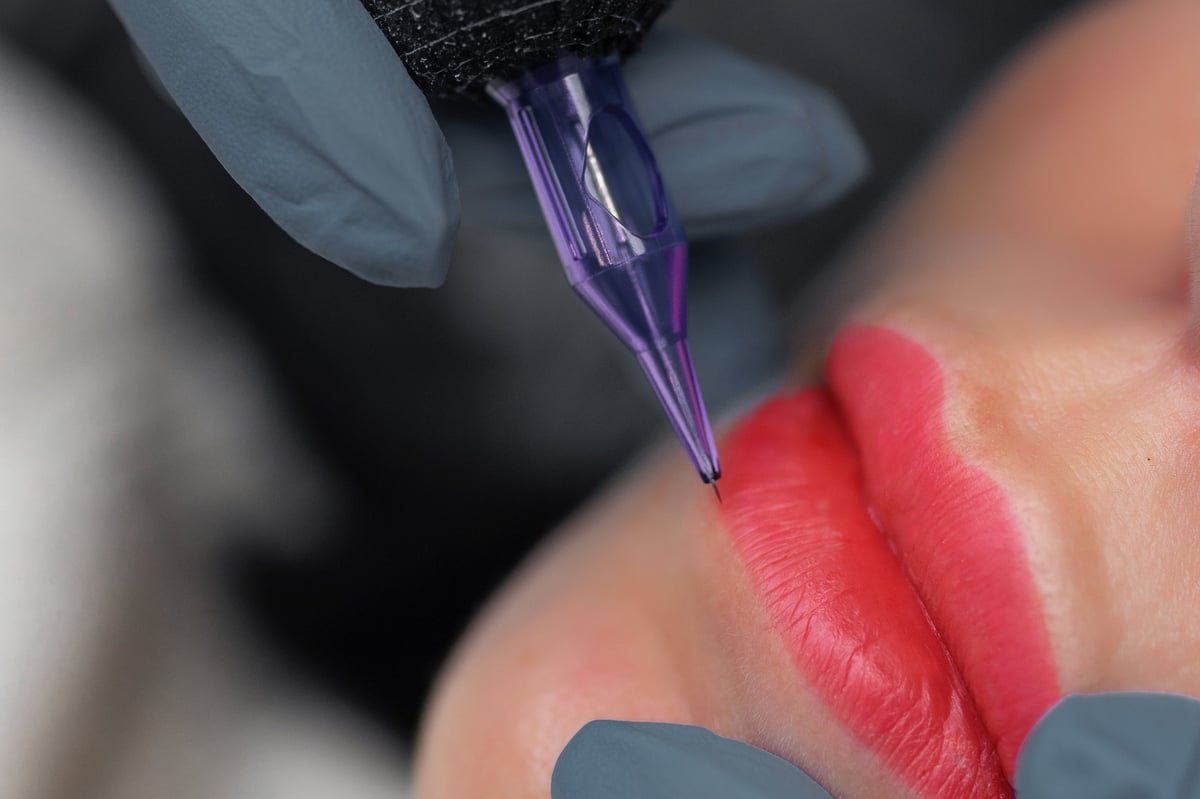 Close up of a cosmetologist performing permanent lip makeup, tattooing natural lip color enhancement with sterile tools in a professional beauty studio