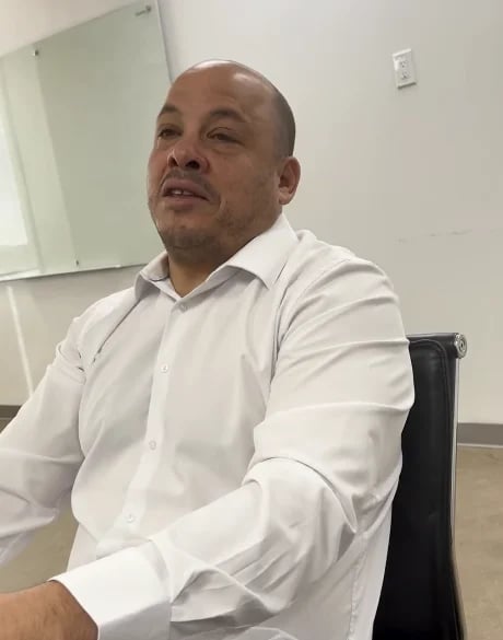 Man in white dress shirt sitting in office chair with whiteboard visible in background